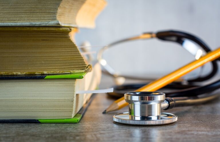 A medical student studying alone at a desk with textbooks, a laptop, and handwritten notes.