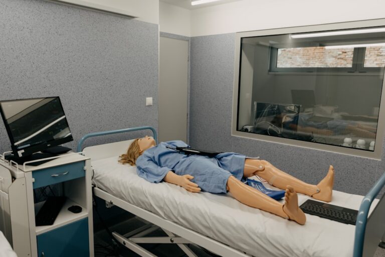 Medical students in white coats practicing clinical skills on simulation mannequins in a classroom lab.